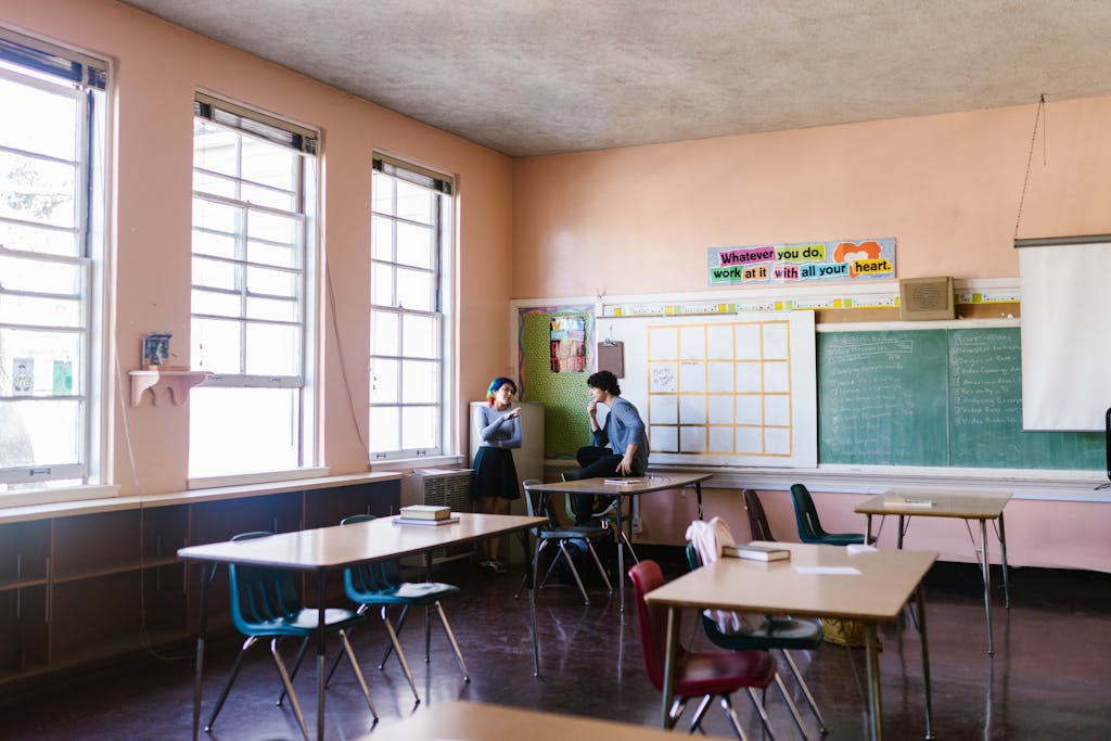 Two students having a conversation in a quiet classroom setting, surrounded by learning materials.